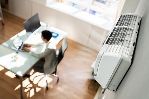 Bird's eye view of an office. An air conditioner is in the foreground and a man sitting at a desk is in the background.