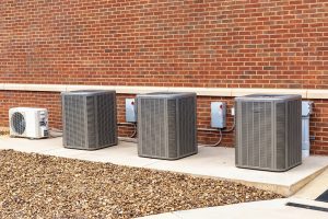 Horizontal shot of commercial heating and air conditioning units installed in commercial building against a brick wall.