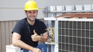AC repair man sitting beside an AC and giving a thumbs up