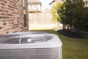 An air conditioner sitting outside of a brick home on a sunny day