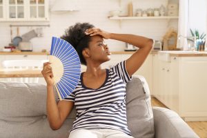 African woman suffer from heat at home use paper fan 