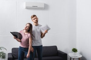 Young couple fanning themselves in front of broken AC unit